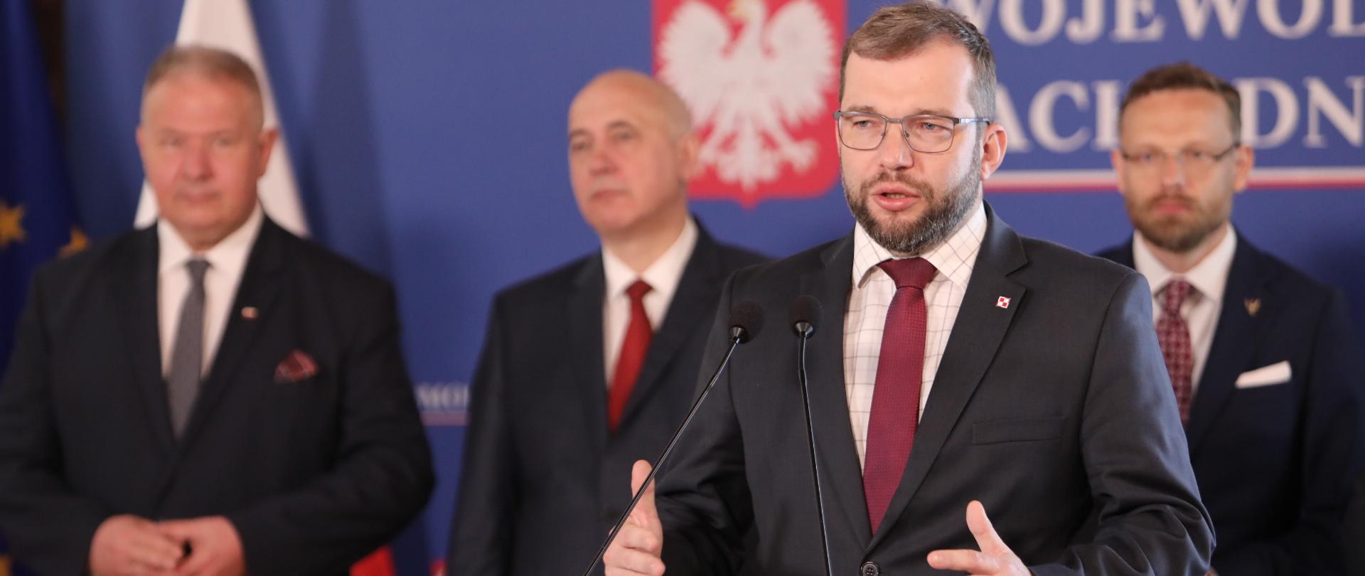 minister Grzegorz Puda przy mównicy, za nim stoją m.in. europoseł Joachim Brudziński i wojewoda Zbigniew Bogucki