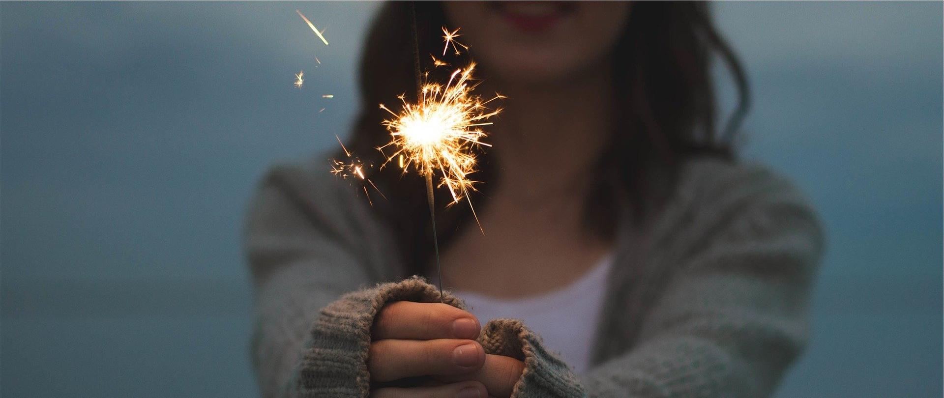 kobieta ubrana w sweter, trzymająca w rękach palące się zimne ognie 