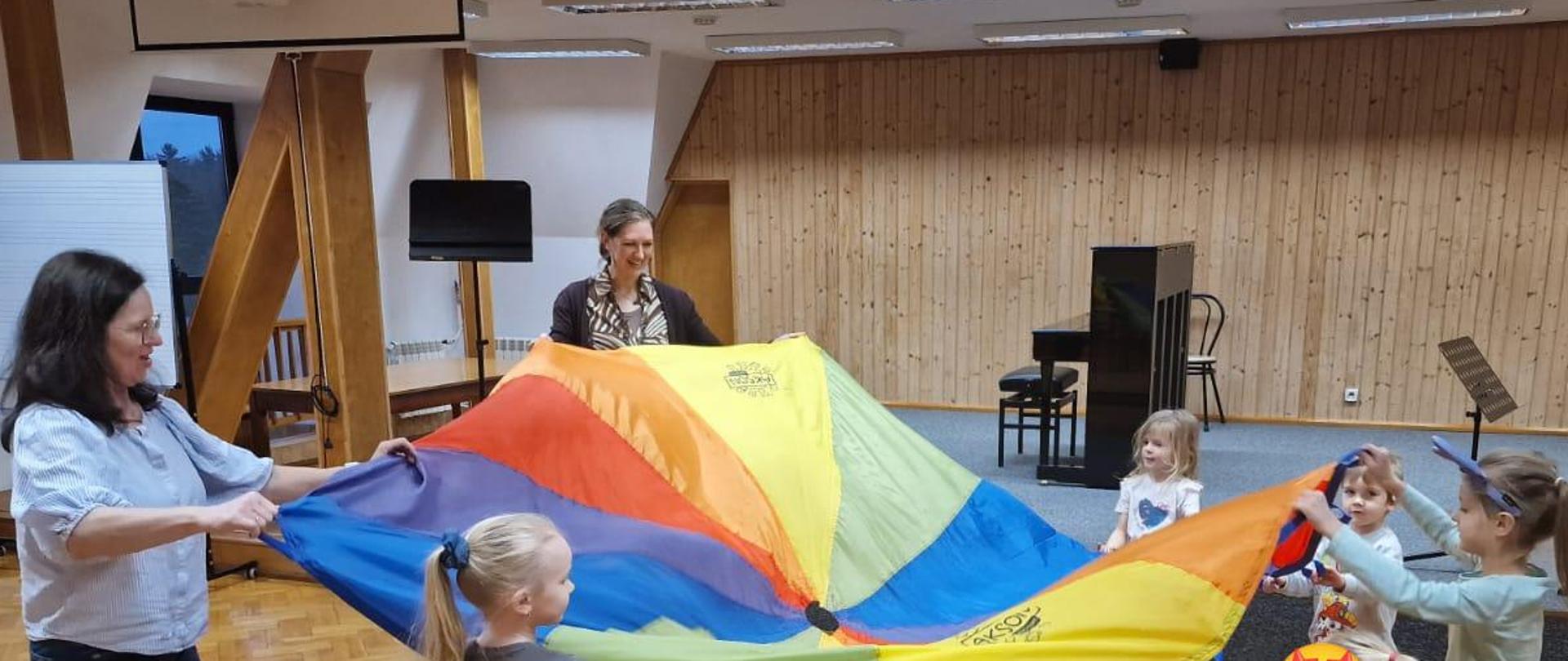 Dwie kobiety i kilkoro dzieci trzymają dużą chustę.