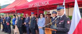 Na zdjęciu przy mównicy na uroczystości 75-lecia OSP Uście Gorlickie oraz poświęceniu i przekazaniu samochodów pożarniczych przemawia zastępca małopolskiego komendanta wojewódzkiego. W tle czerwone namioty i zaproszeni na uroczystość goście mundurowi i cywile.