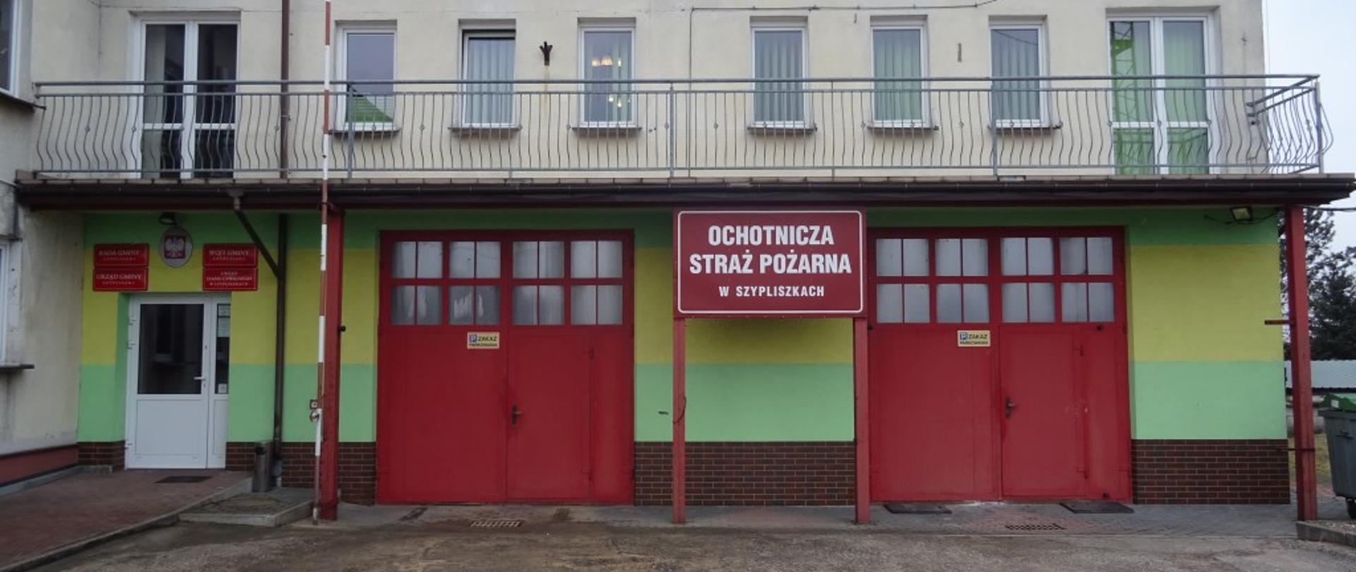 Widoczny budynek z dwiema kondygnacjami. Na całej długości pierwszego piętra znajduję się balkon z metalowa barierką. Dwie bramy koloru czerwonego. Po lewej stronie wejście do budynku. Podjazd przed garaże wylany asfaltem. 