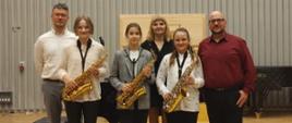 Zdjęcie przedstawia stojących na scenie trzymających saksofony trzech uczniów biorących udział w EFS wraz z nauczycielem Adrianem Masselim i akompaniatorami - naucz. Marią i Danielem Rybakami