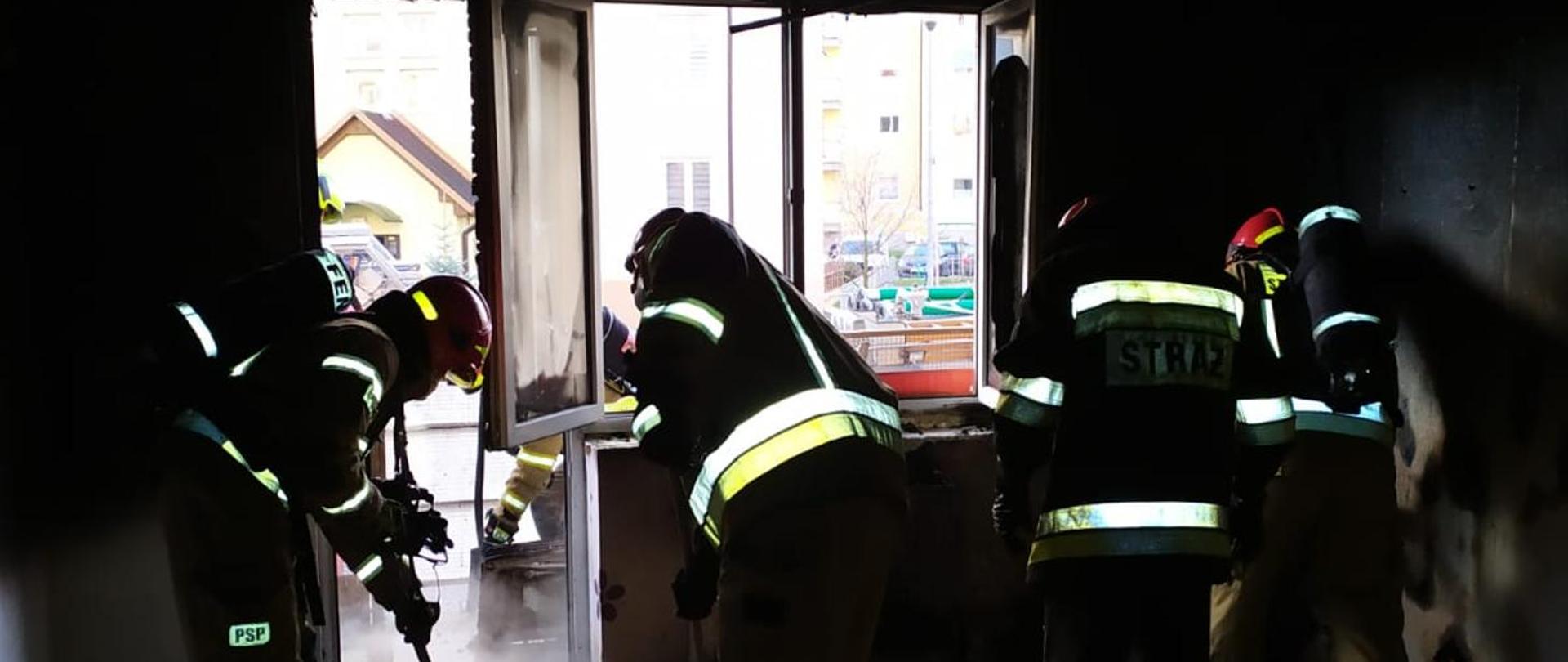 Fotografia przedstawia strażaków oczyszczających pomieszczenie z resztek po pożarowych.