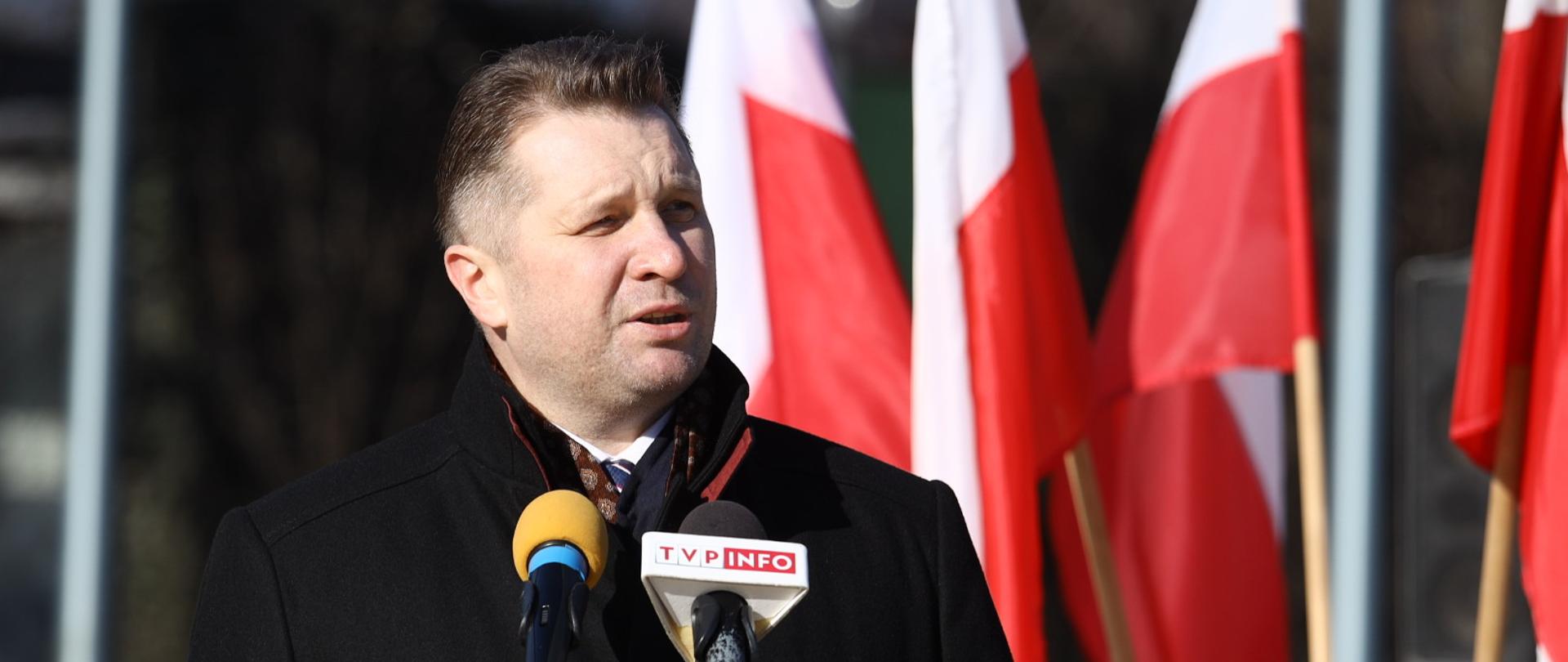 Minister Przemysław Czarnek przemawia podczas uroczystości w Lublinie z okazji 80. rocznicy utworzenia Armii Krajowej ujęcie z bliska. widać jedynie ministra i mikrofony oraz żołnierza, który stoi po prawej stronie ministra. Minister Przemysław Czarnek wziął udział w lubelskich obchodach 80. rocznicy utworzenia Armii Krajowej 