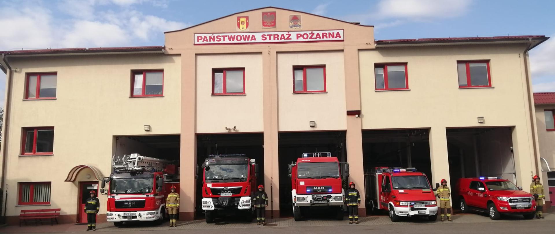 Funkcjonariusze salutują na tle KP PSP w Człuchowie.