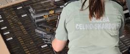 Funkcjonariuszka Służby Celno-Skarbowej w czarnych rękawiczkach przy zabezpieczonych papierosach.