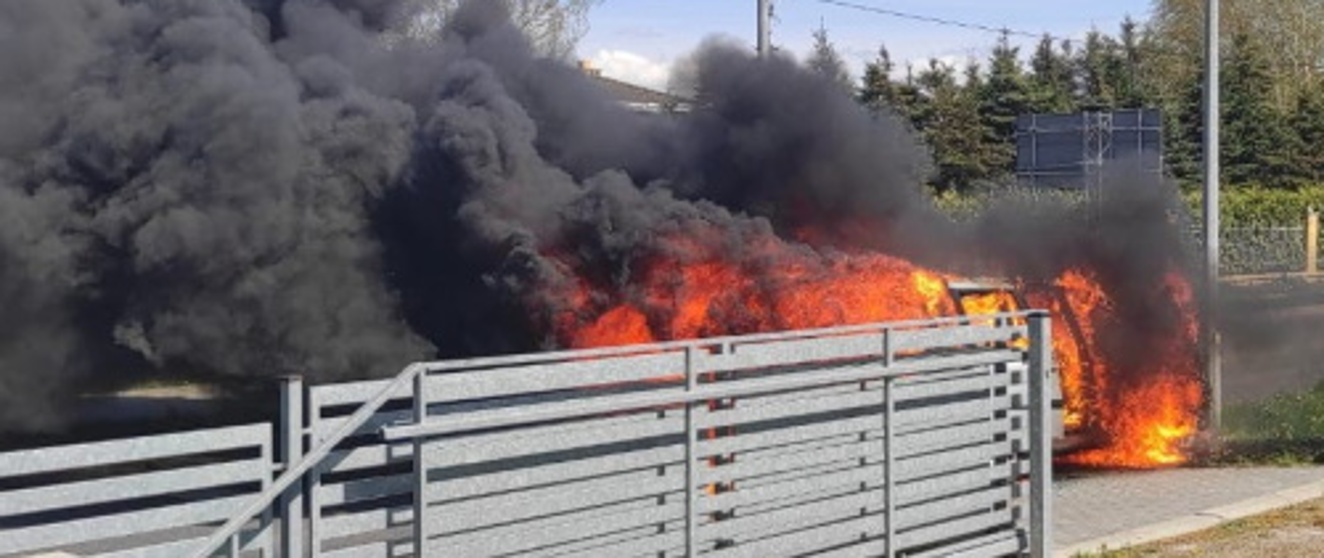 Za płotem samochód w płomieniach i duże zadymienie
