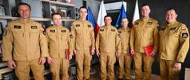 Wspólne zdjęcie pamiątkowe siedmiu oficerów PSP w piaskowych mundurach. Stoją w jednym rzędzie na tle flag i regału z pucharami. Od lewej: st. bryg. Adam Wiśniewski, kpt. Artur Barański, st. kpt. Paweł Krzyśko, nadbryg. Tomasz Baran, mł. bryg. Marek Rusnarczyk, mł. bryg. Tomasz Pustelak oraz st. bryg. Dariusz Homa.