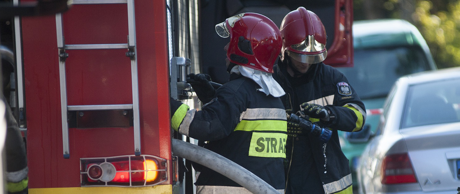 Dwóch strażaków Państwowej Straży Pożarnej przy wozie strażackim.