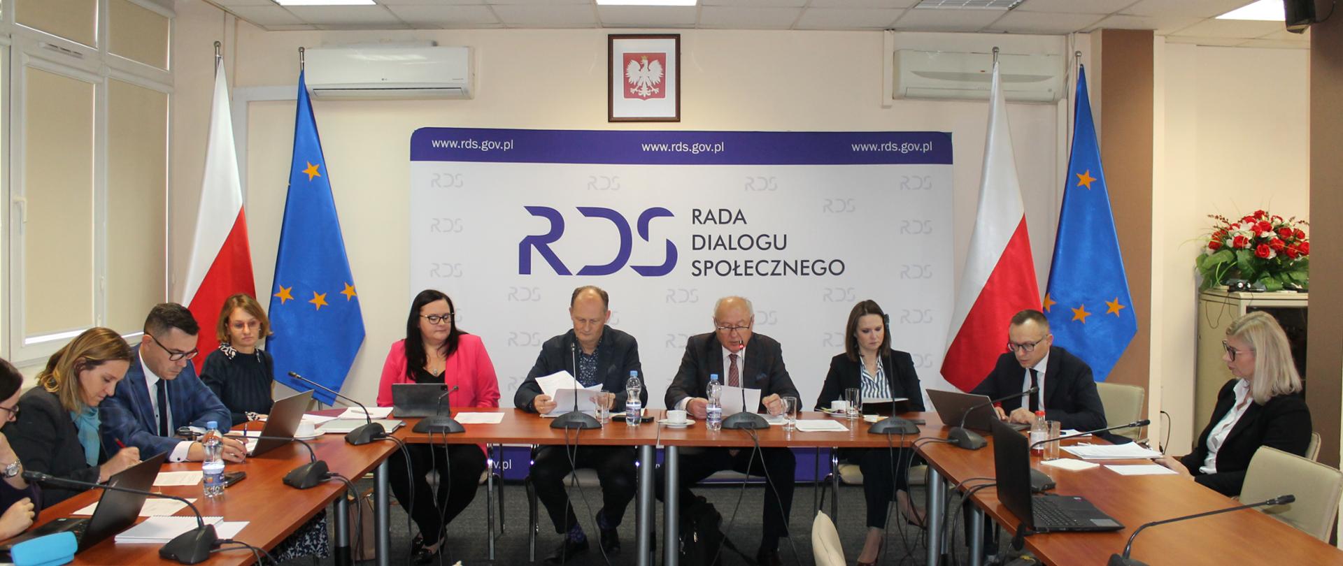 Zdjęcie przedstawia stół prezydialny za którymi siedzi od lewej strony: Małgorzata Jarosińska-Jedynak – Sekretarz Stanu w Ministerstwie Funduszy i Polityki Regionalnej, Norbert Pruszanowski – Związek Rzemiosła Polskiego, Jan Klimek – Przewodniczący Zespołu, Anna Schmidt – Sekretarz Stanu w Ministerstwie Rodziny i Polityki Społecznej oraz Artur Soboń – Sekretarz Stanu w Ministerstwie Finansów. W tle osób baner z napisem Rada Dialogu Społecznego. Po lewej i prawej stronie stoją po dwie flagi: Polski i UE. Nad banerem wisi godło Polski.