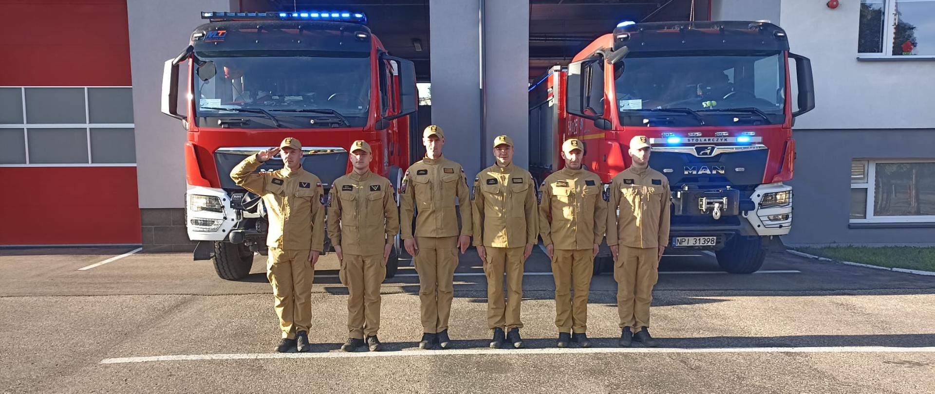 Strażacy salutujący na tle samochodu pożarniczego.