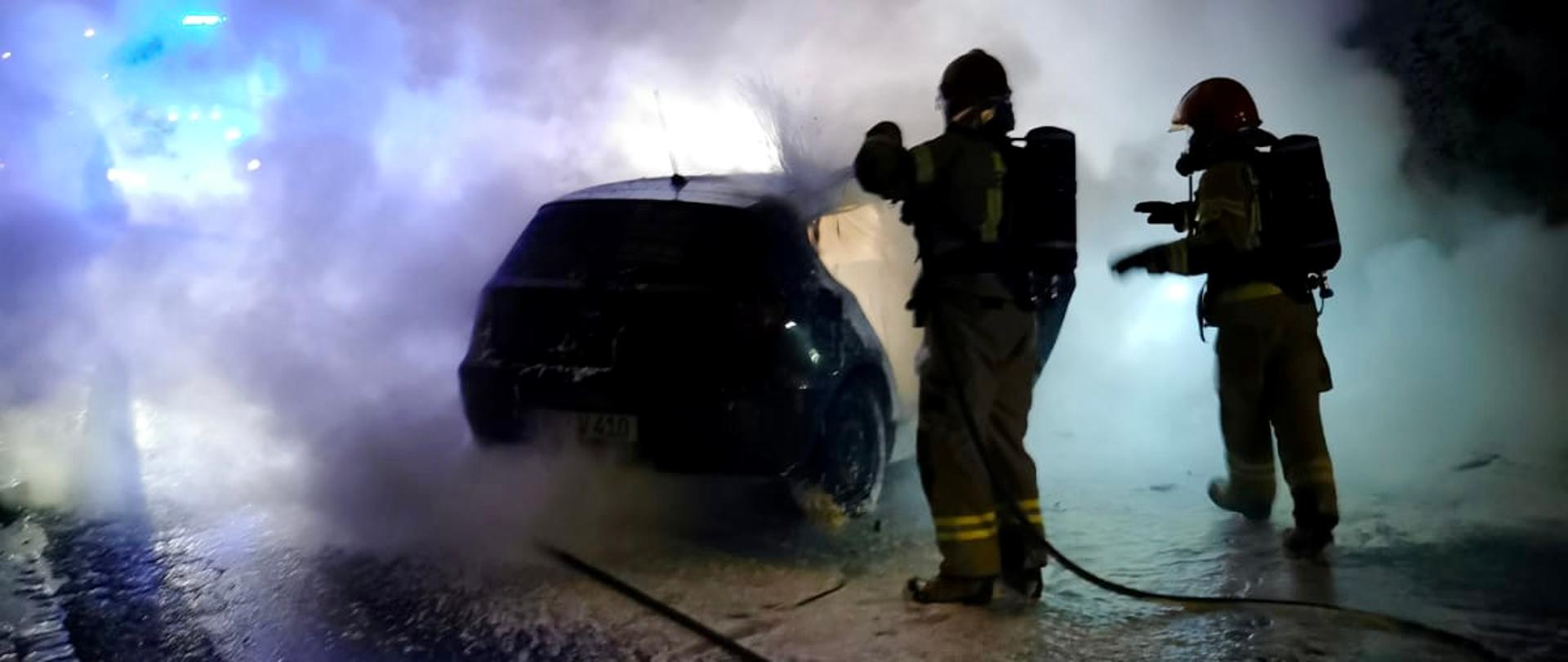 nocna pora, strażacy gaszący palący się samochód w kłębach dymu