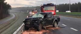 Samochód osobowy po uderzeniu w tył samochodu ciężarowego. Widać znaczne uszkodzenia przodu pojazdu. Za nim stoją dwa samochody strażackie. Ruch na trasie S7 odbywa się prawidłowo. 
