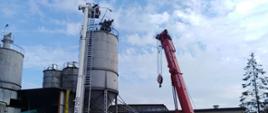 Na zdjęciu widzimy strażacki podnośnik i strażacki dźwig, pracujące przy silosie z cementem.