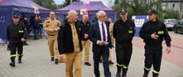 Wizyta Wiceministra Spraw Wewnętrznych i Administracji oraz kadry PSP u druhów ochotników - wiceminister i strażacy PSP podczas rozmowy w garażu OSP z druhami, w tle namioty Gminy Choroszcz