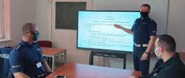 Zdjęcie przedstawia funkcjonariusza policji prowadzącego wykład z użyciem ekranu multimedialnego