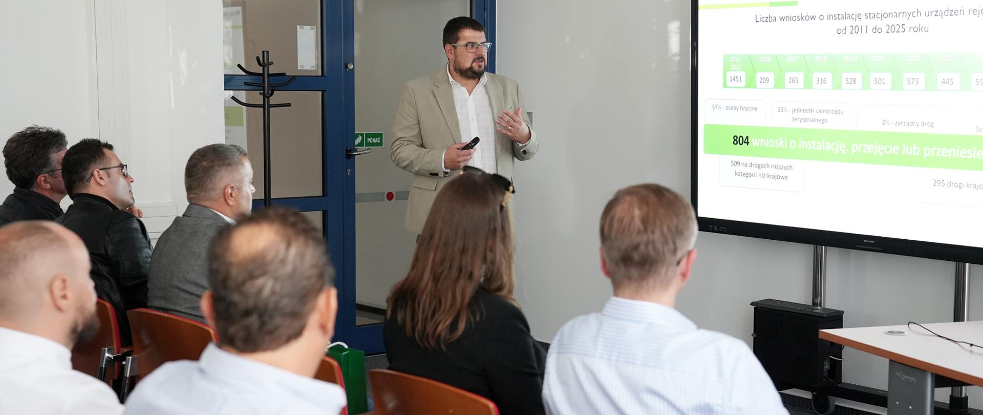 Prelegent w jasnej marynarce przedstawia dane dotyczące wniosków o objęcie nadzorem przez CANARD. Uczestnicy siedzą przed ekranem prezentacyjnym w sali konferencyjnej.