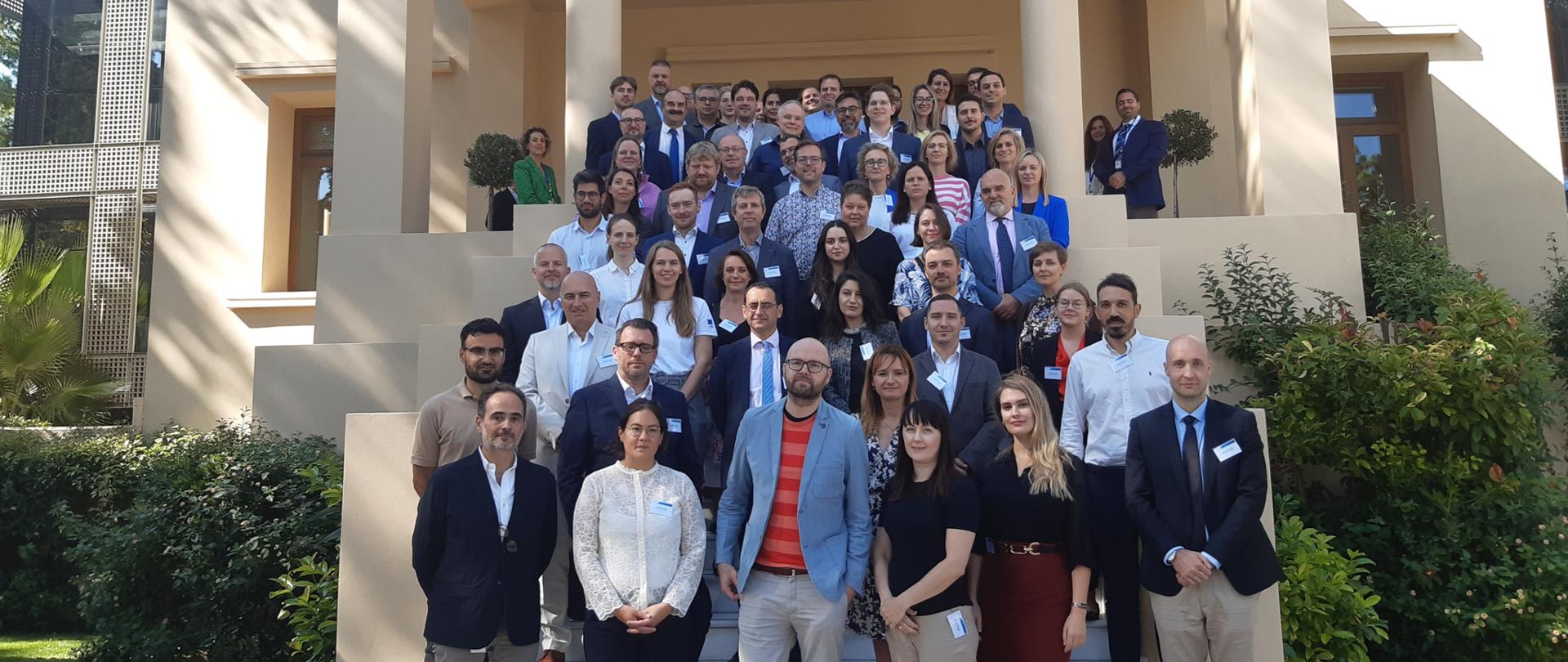 Zdjęcie przedstawia przedstawicieli sieci NCC's, Komisji Europejskiej oraz Agencji Unii Europejskiej ds. Cyberbezpieczeństwa (ENISA) stojących na tle siedziby ENISA w Atenach 