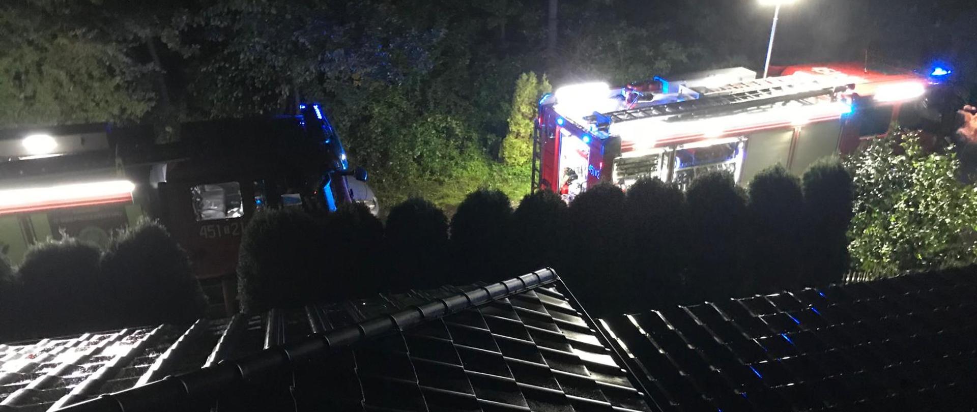 Na zdjęciu dwa samochody strażackie. Kadr zrobiony z dachu domu mieszkalnego w porze nocnej.