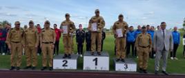 Strażacy podczas dekoracji zwycięzców mistrzostw pożarniczych stoją przy podium na stadionie