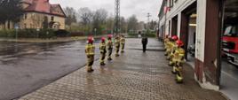 Zdjęcie przedstawia strażaków podczas uroczystej zmiany służby na placu zewnętrznym Jednostki Ratowniczo-Gaśniczej. Strażacy stojący w szeregu naprzeciw siebie. Zmiany służbowej dokonuje dowódca Jednostki Ratowniczo-Gaśniczej. 