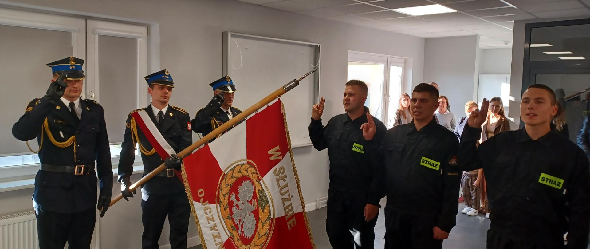 str. Filip Czapiewski, str. Michał Jankowski i str. Nikodem Szmurło (od lewej) składają ślubowanie. Po lewej stronie poczet sztandarowy, w tle rodziny nowych funkcjonariuszy.