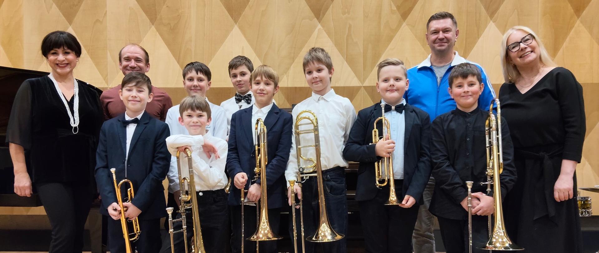 Grupa trębaczy i puzonistów z nauczycielami na scenie sali koncertowej PSM
