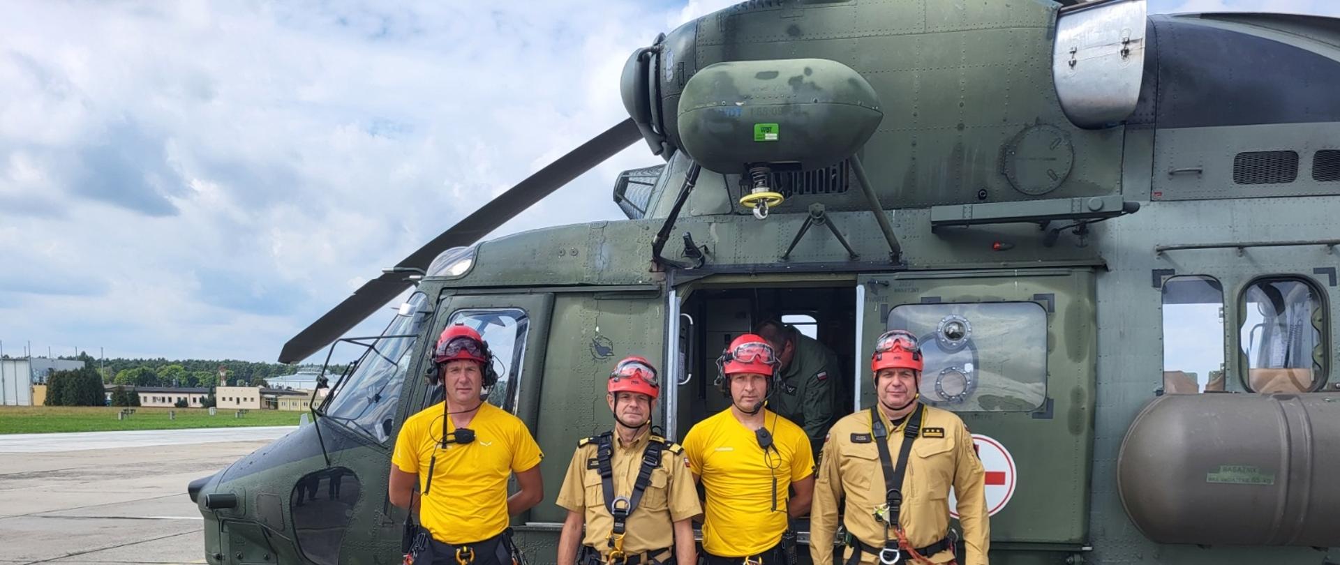 Strażacy i żołnierze pozujący do zdjęcia na płycie lotniska ze śmigłowcem w tle.