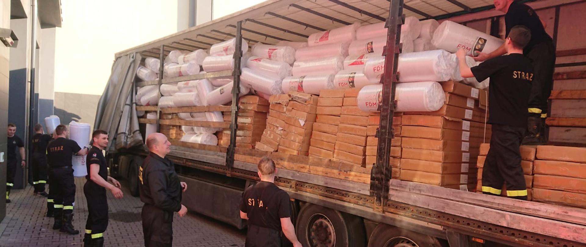 Strażacy rozładowują łózka i materace z samochodu ciężarowego.