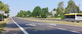 zdjęcie drogi krajowej nr 94 w Olkuszu. Widoczne dwie jezdnie po dwa pasy ruchu w obu kierunkach z oznakowaniem poziomym i pionowym. Jezdnie oddzielone są pasem zieleni i barierami ochronnymi. 