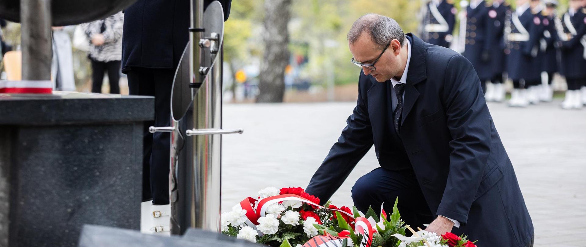 Mężczyzna kładzie wieniec z biało czerwoną szarfą przed pomnikiem Ofiar Zbrodni Katyńskiej