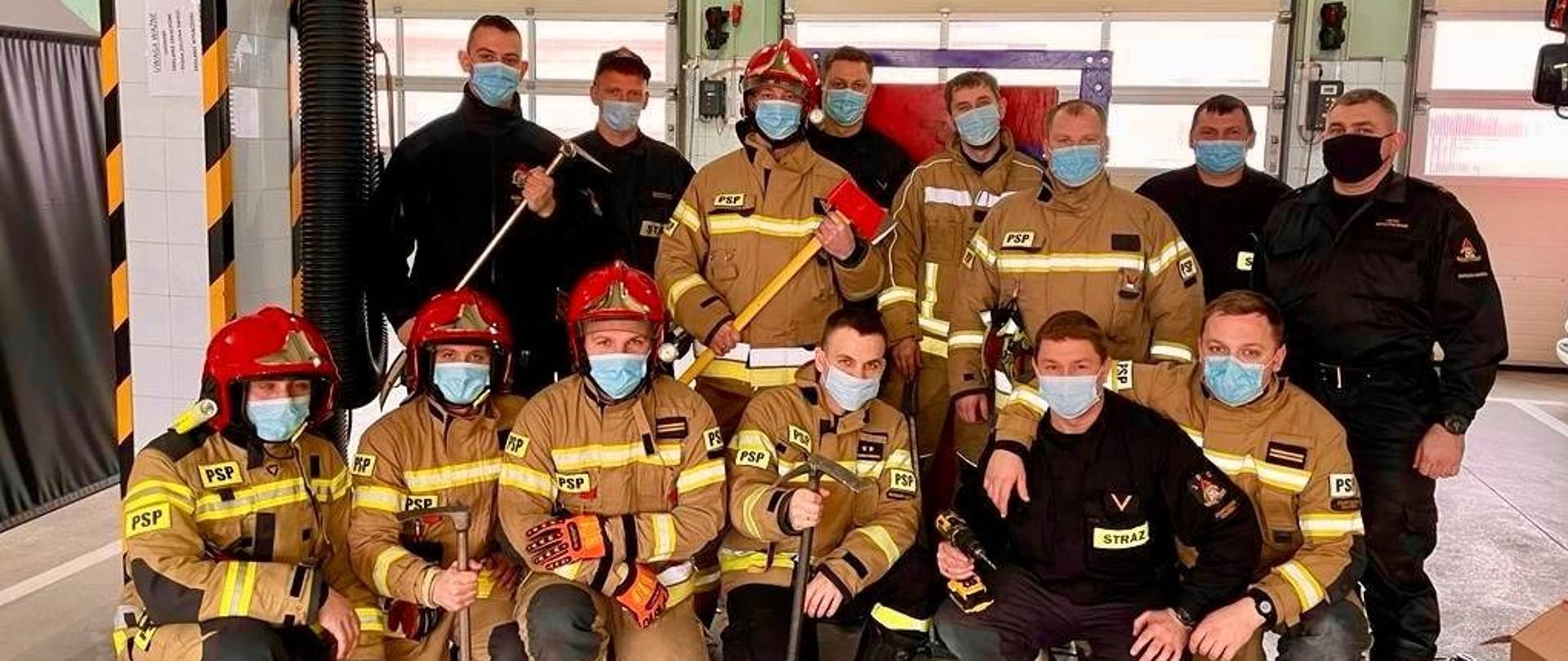 Zdjęcie przedstawia uczestników warsztatów, część strażaków w hełmach, trzymają narzędzia pożarnicze