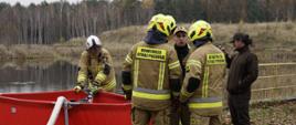 Strażacy OSP przygotowują przenośny zbiornik wodny, stanowiący element stanowiska szkoleniowego poświęconego organizacji punktu czerpania wody. Na pierwszym planie widać montaż i podłączenie węży tłocznych, a w tle – brzeg zbiornika Kozieławy oraz instruktorów nadzorujących pracę. Ćwiczenia obejmowały zarówno technikę ustawiania zbiornika, jak i zasady bezpiecznego zasilania linii gaśniczych.