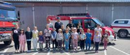 Dzieci oraz strażacy PSP i OSP pozują do zdjęcia. W tle samochody strażackie.