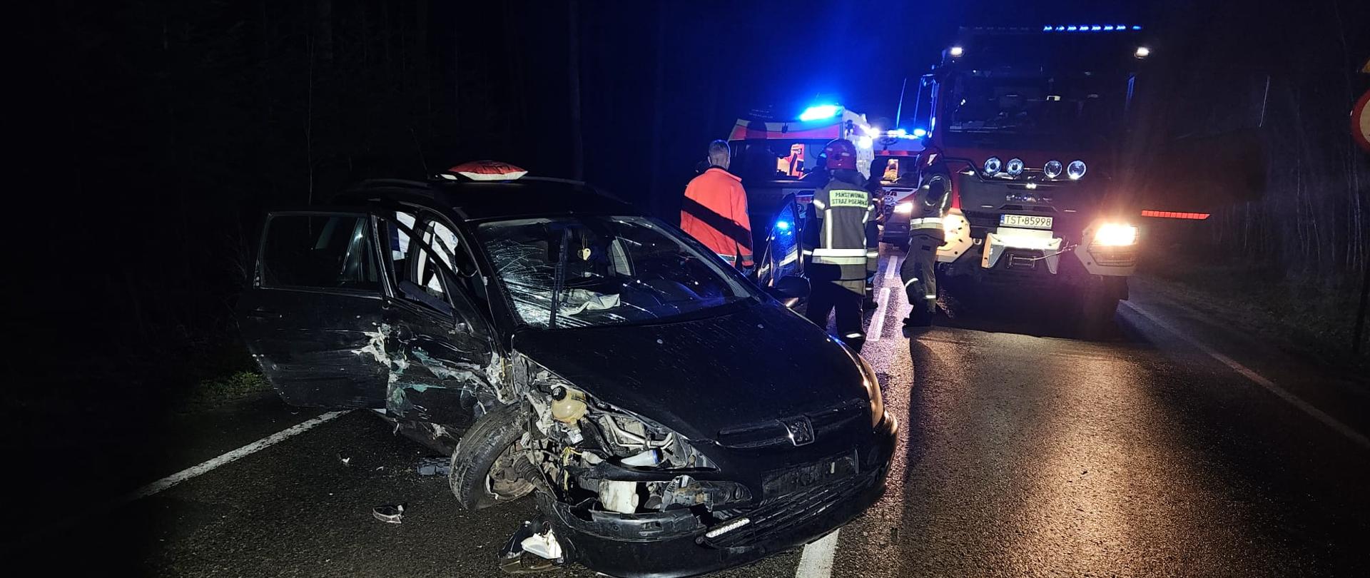 Samochód osobowy z uszkodzonym przodem na jezdni w tle służby ratownicze. Pora nocna.