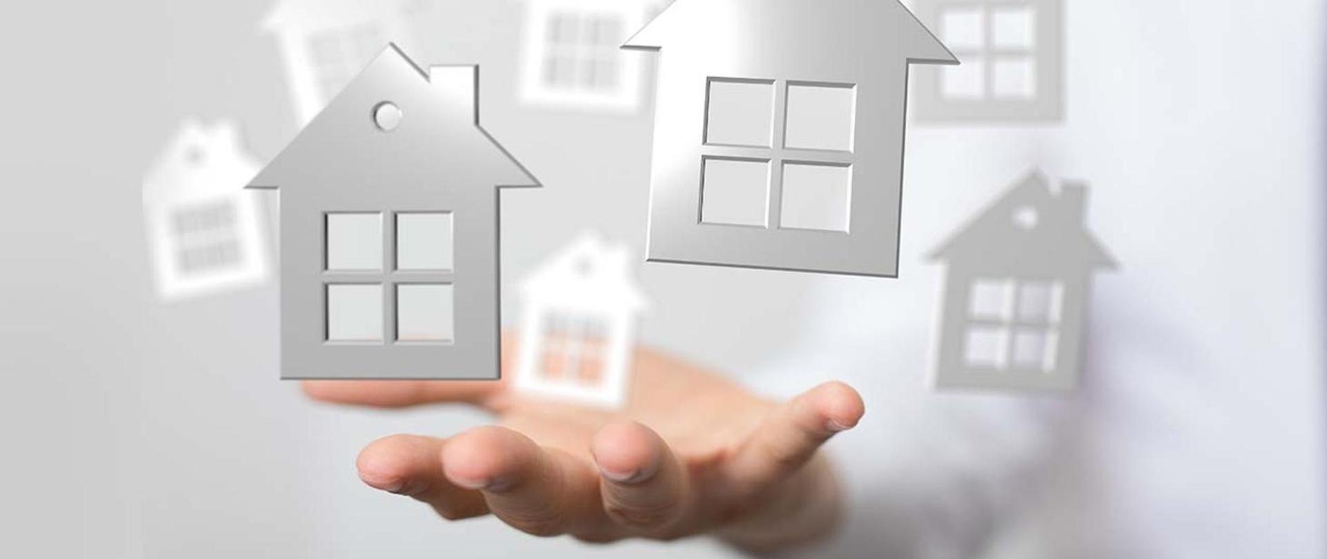 Grafika przedstawia dłoń, która podtrzymuje zarysy domów