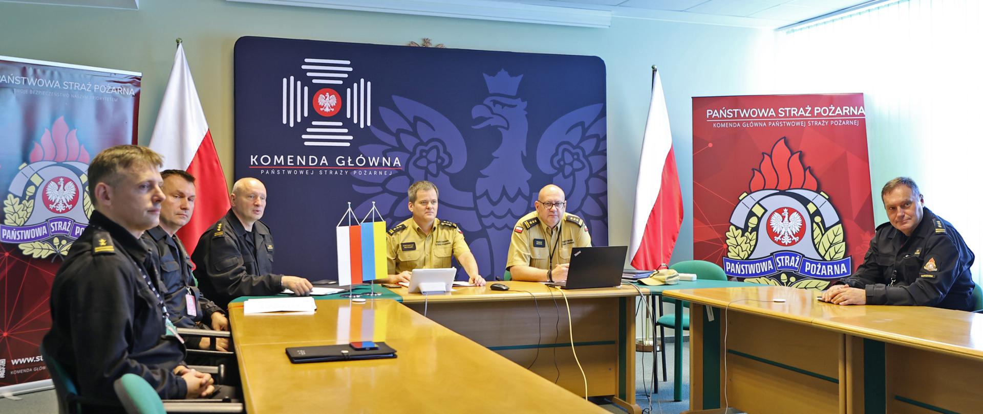 Sześciu mężczyzn w strażackich mundurach siedzących przy stole w trakcie wideokonferencji