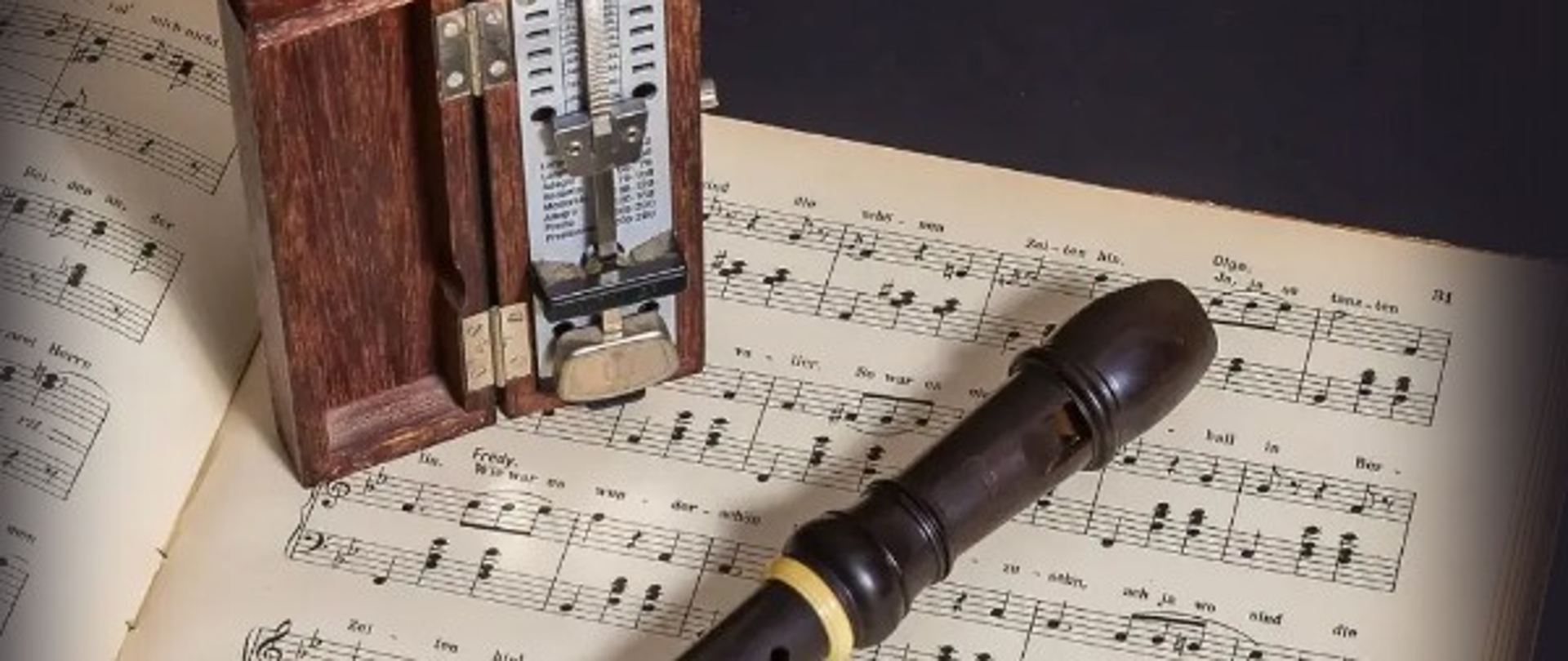 Plakat zapowiadający popis klasy fletu. Na górze widnieje duży napis „Popis klasowy klasy fletu Pani Elżbiety Sawickiej”, poniżej tekst „Zapraszamy bardzo serdecznie”. Po prawej stronie zamieszczono datę i godzinę wydarzenia: „01.12.2025, godzina 17.00, Sala koncertowa”. W dolnej części plakatu znajduje się zdjęcie otwartego metronomu w drewnianej obudowie, leżącego na rozłożonych nutach, obok którego umieszczono flet prosty w ciemnym kolorze. Całość utrzymana jest w eleganckiej, stonowanej stylistyce.