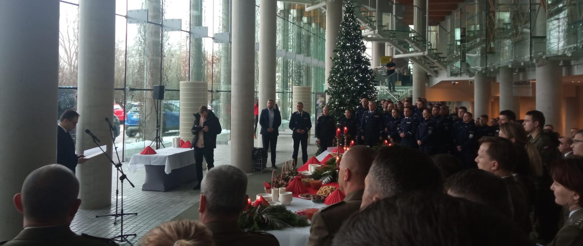 W pomieszczeniu stoi kilkadziesiąt osób w różnych mundurach. Ze nimi wielka choinka.