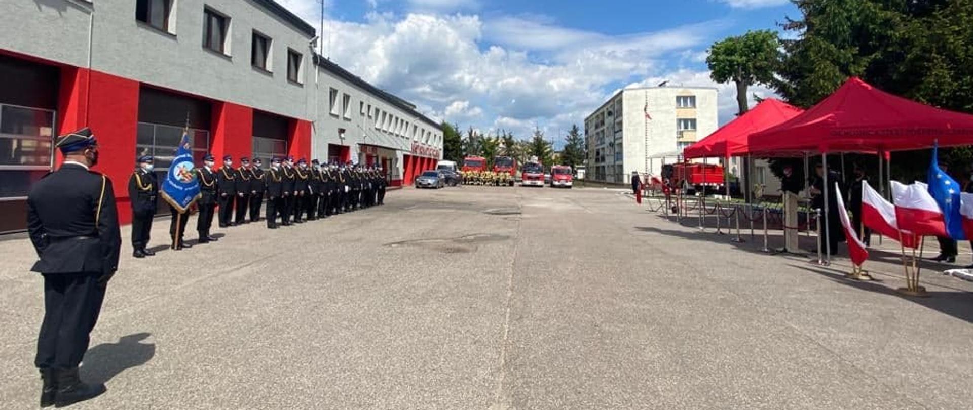 Zbiórka na placu wewnętrznym KP PSP w Makowie Mazowieckim. Pododdział stoi przed budynkiem naprzeciw zaproszonych gości.