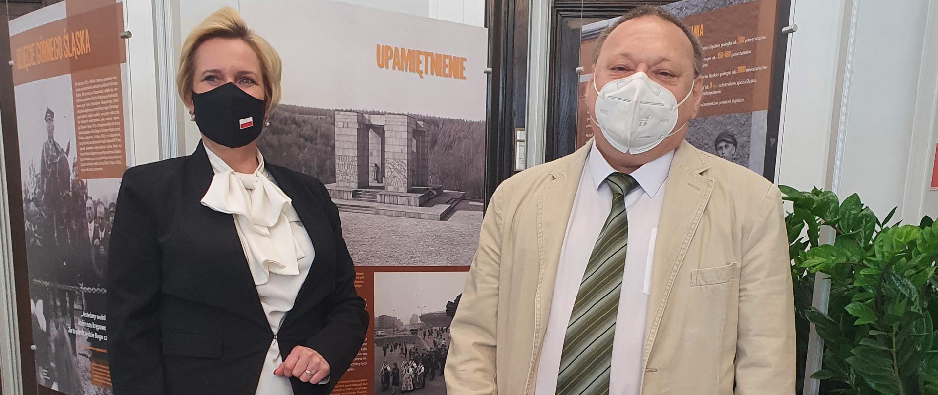 Wystawa „Powstania śląskie 1919−1921” w Senacie RP. Na zdjęciu wicewojewoda opolski oraz senator Jerzy Czerwiński. Zdjęcie zrobiono w pionie. Po lewej stronie stoi wicewojewoda, ubrana w czarną garsonkę. Jej lewa ręka jest nieco zgięta w łokciu. Po przeciwnej stornie stoi ubrany w jasny garnitur senator, na szyi ma zielony krawat. W tle widać plansze wystawy dot. III Powstania Śląskiego. 