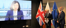 Marek Zagórski, minister cyfryzacji i Jonathan Knott - brytyjski ambasador w Polsce przemawiają do mikrofonów. W tle flagi Wielkiej Brytanii, Polski i UE. Na ekranie wideo z przemówienia Very Jorovej, komisarz UE ds. sprawiedliwości, spraw konsumenckich i równości płci.