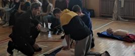 Pokaz udzielania RKO przez strażaka, wokół uczniowie, zdjęcie wykonane na sali gimnastycznej. 