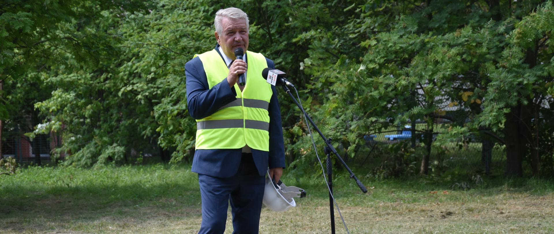 Na zdjęciu znajduje się mężczyzna przemawiający do mikrofonu