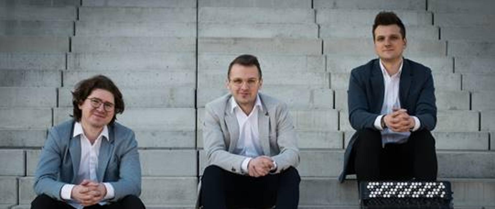 Zdjęcie przedstawia trzech akordeonistów siedzących na schodach wraz ze swoimi instrumentami.