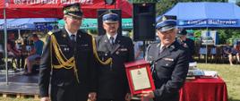 dwóch strażaków oraz druh w mundurach galowych pozują do zdjęcia, za nimi namioty wystawowe 