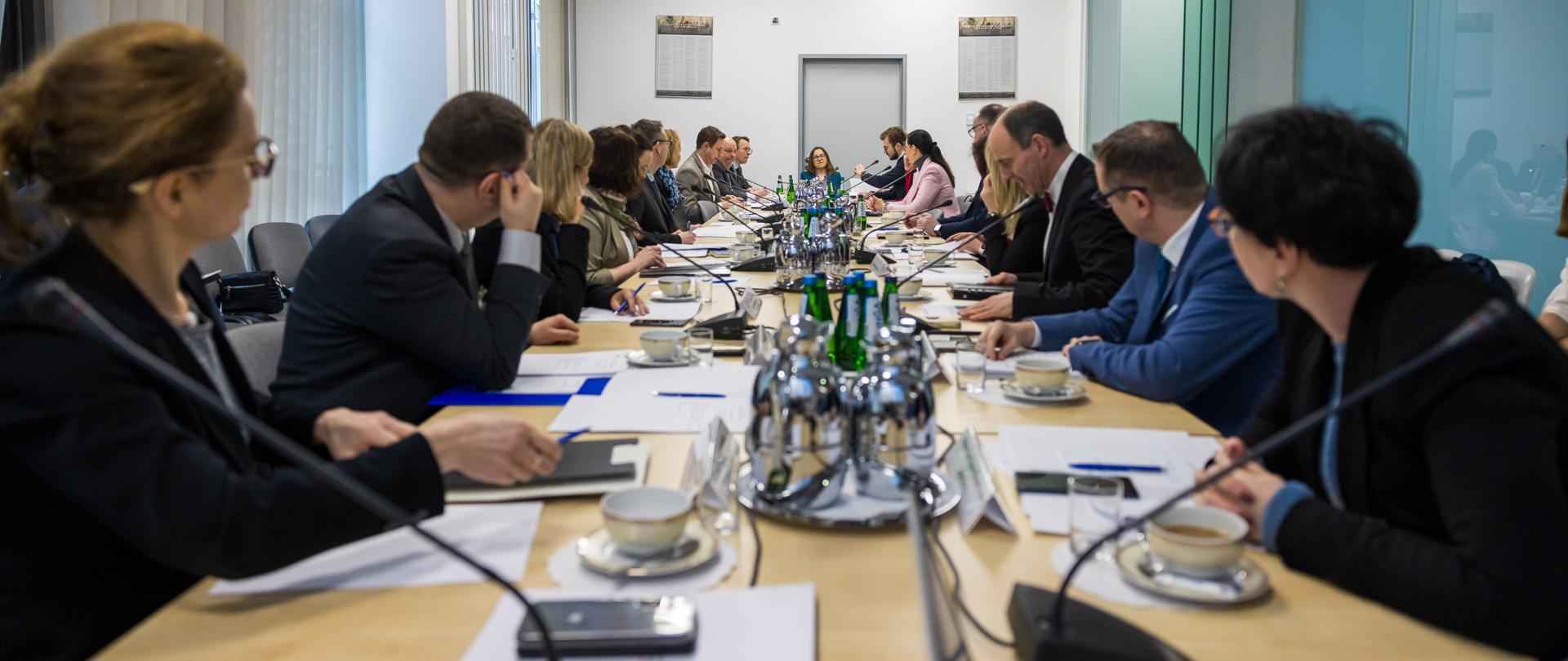 A diverse group of individuals sitting at a lengthy table, engaged in a discussion or meeting.