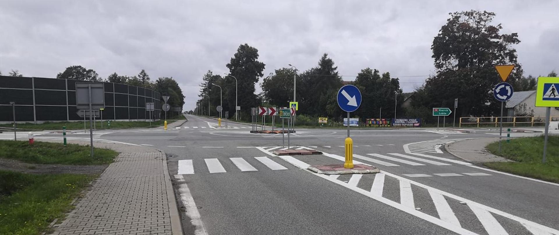 Skrzyżowanie DK74 w Zawadzie - na środku skrzyżowania z ruchem okrężnym mała wysepka z pionowymi elementami oznakowania (czerwone strzałki na białym tle). Na czterech wlotach na skrzyżowanie przejścia dla pieszych z azylami. między pasami ruchu. Wokół skrzyżowania znaki i drogowskazy.