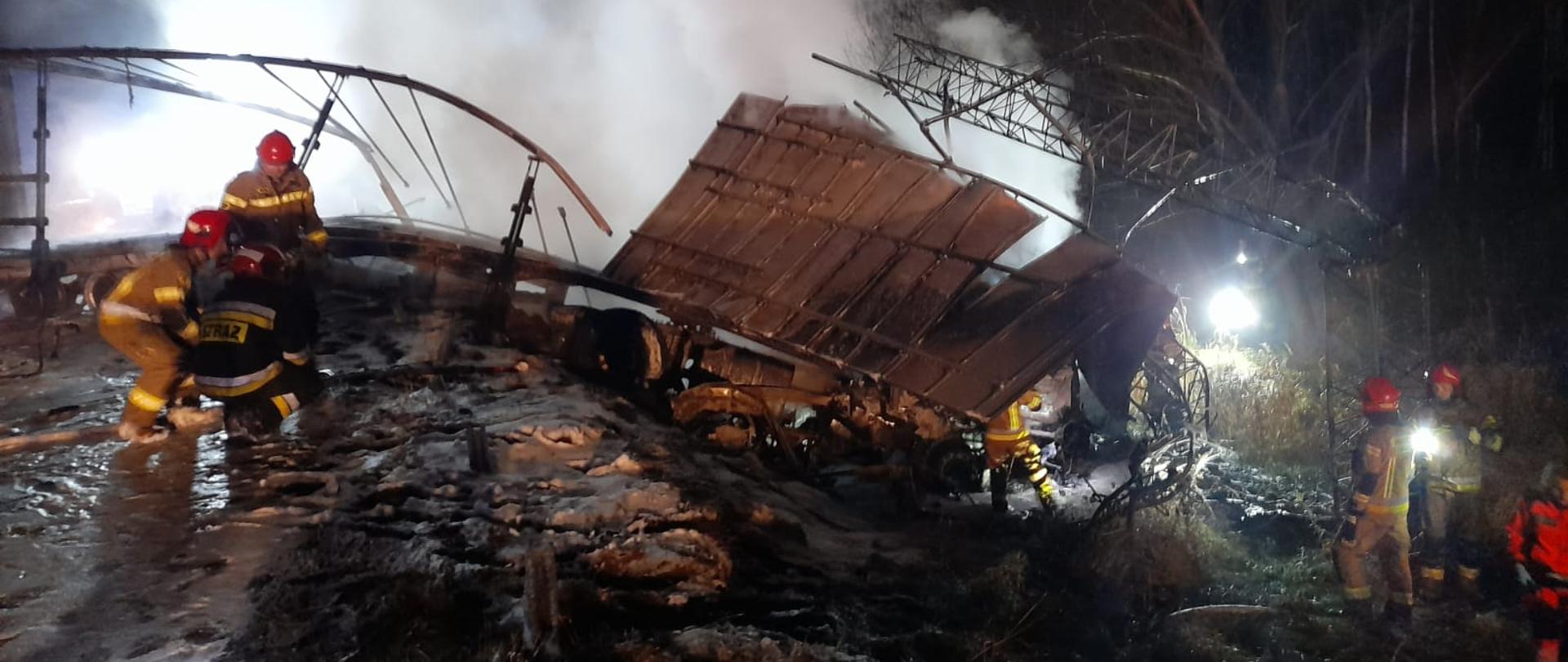 Strażacy sprawdzają wrak spalonej naczepy.