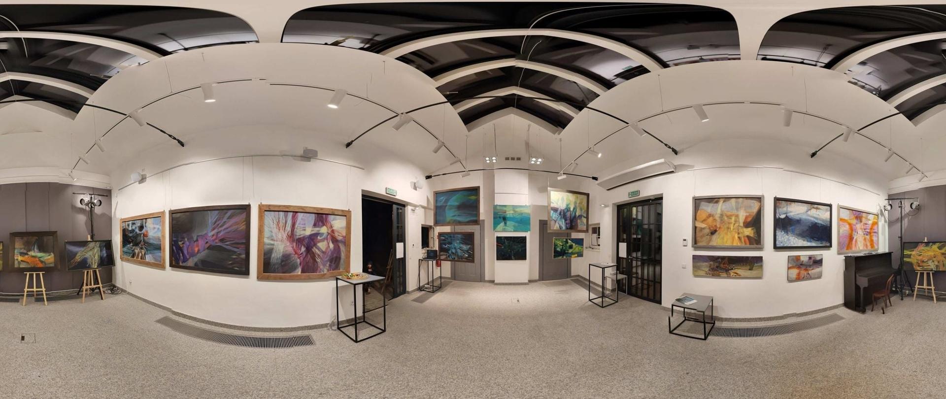 Wystawa malarstwa J. Pęczuły. Obrazy wiszą na ścianach w galerii. Obraz fotografii jest zniekształcony.